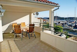 A balcony with two chairs and a table, overlooking a marina with boats and a hilly landscape. - Apartments Marina View (Tribunj)