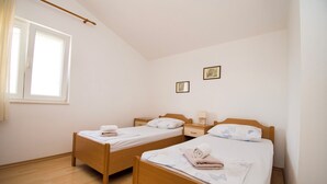 Ein Zimmer mit zwei Holzbett, einem fenster mit Vorhängen und zwei gerahmten Bildern an der Wand.