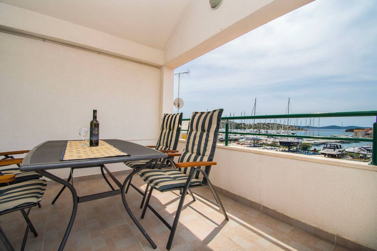 A balcony with a table and chairs, overlooking a marina with boats.
