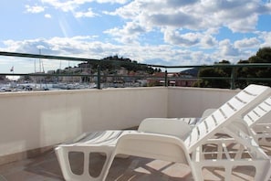 A terrace with white plastic chairs and a view of a marina with boats and buildings in the background. - Apartments Marina View (Tribunj)