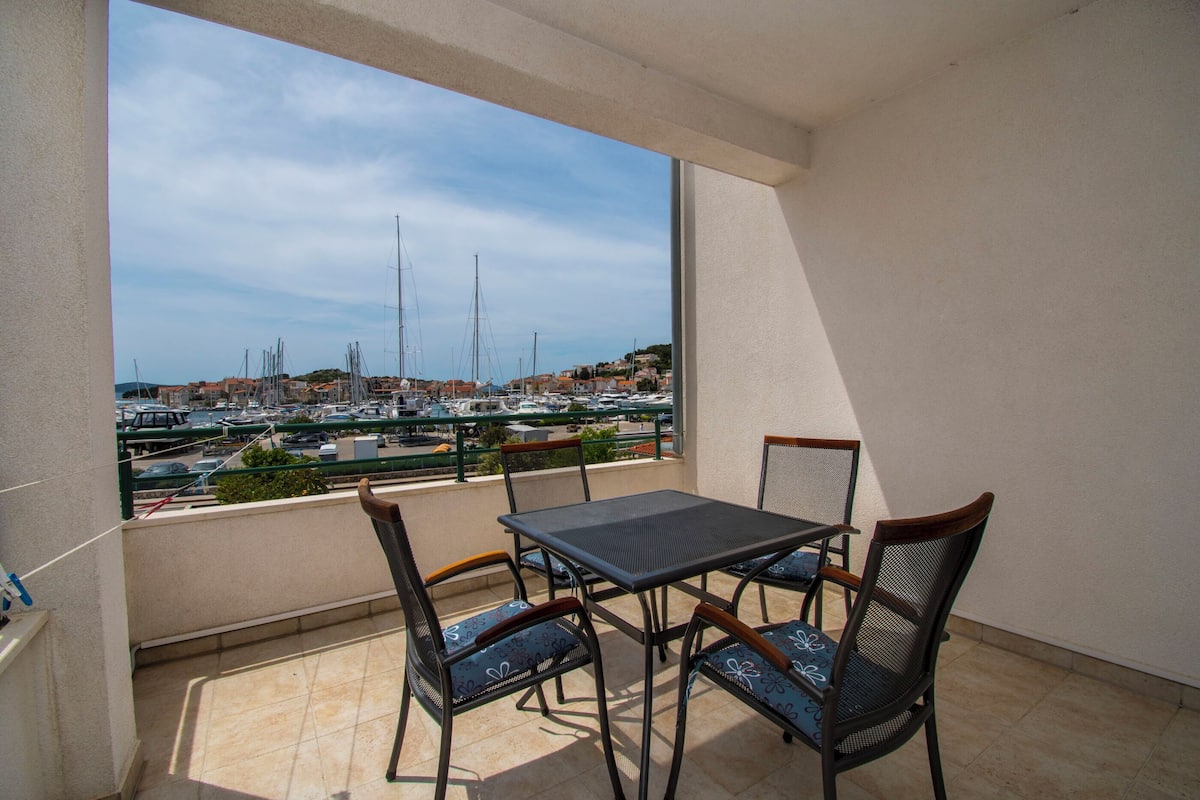 A balcony with a table and chairs, overlooking a marina with boats and buildings.