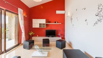 Uma sala de estar moderna com uma parede de destaque vermelha, uma televisão de tela plana e uma mesa de centro de vidro.