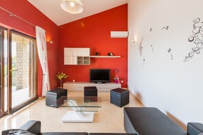 A modern living room with a red accent wall, a flat-screen TV, and a glass coffee table. - Villa Bali (Kastelir-Labinci)