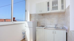 A small kitchen with white cabinets, a built-in sink, and a window overlooking a cityscape. - Apartments Aurora Adriatica (Gradac)