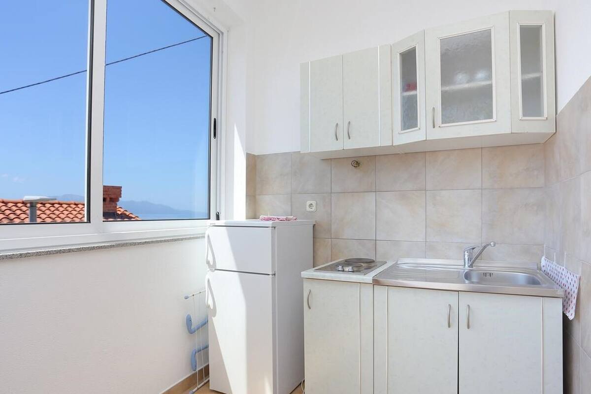 A small kitchen with white cabinets, a built-in sink, and a window overlooking a cityscape.