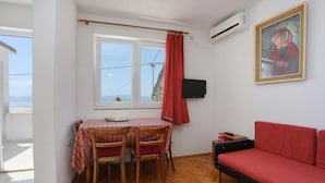 A room with a dining table, two chairs, a red sofa, a TV, and a window with a view of the sea. - Apartments Aurora Adriatica (Gradac)