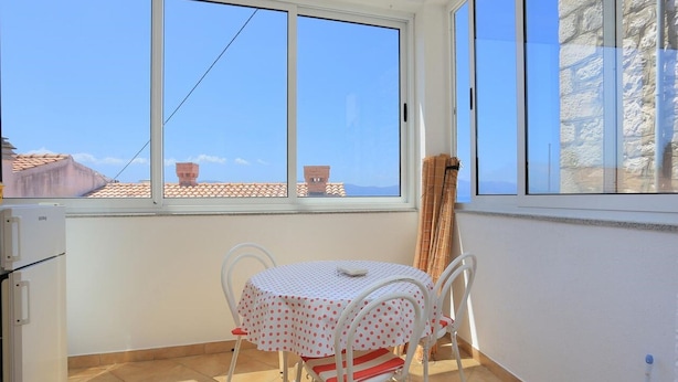 A small balcony with a table and chairs, a window with a view of buildings, and a stone wall. - Apartments Aurora Adriatica (Gradac)