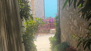 A narrow stone pathway flanked by potted plants and a red gate, leading to a stone building with a tiled roof. - Apartments Aurora Adriatica (Gradac)