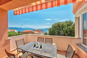 Ein Balkon mit Tisch und Stühlen, der einen schönen Ausblick auf Häuser und Berge bietet.