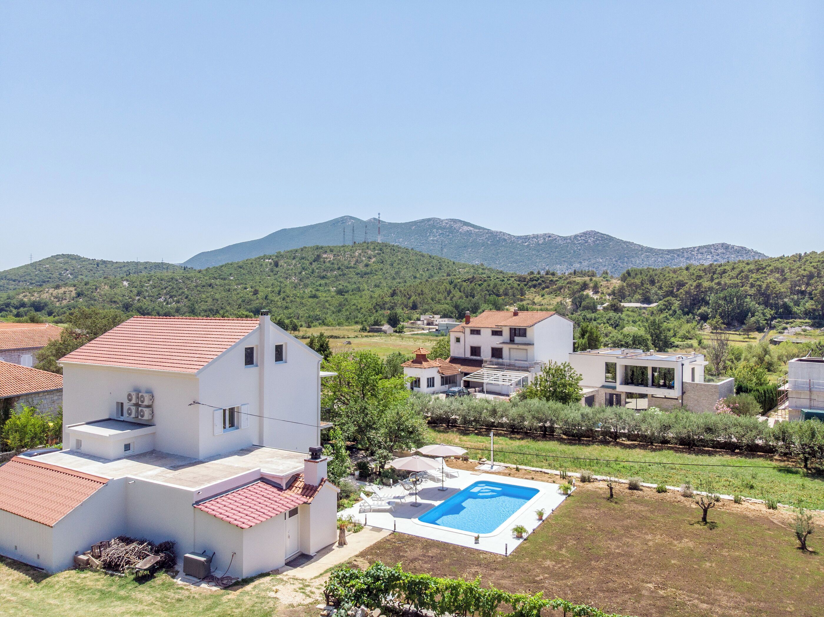 A residential area with houses, a swimming pool, and a mountainous backdrop.