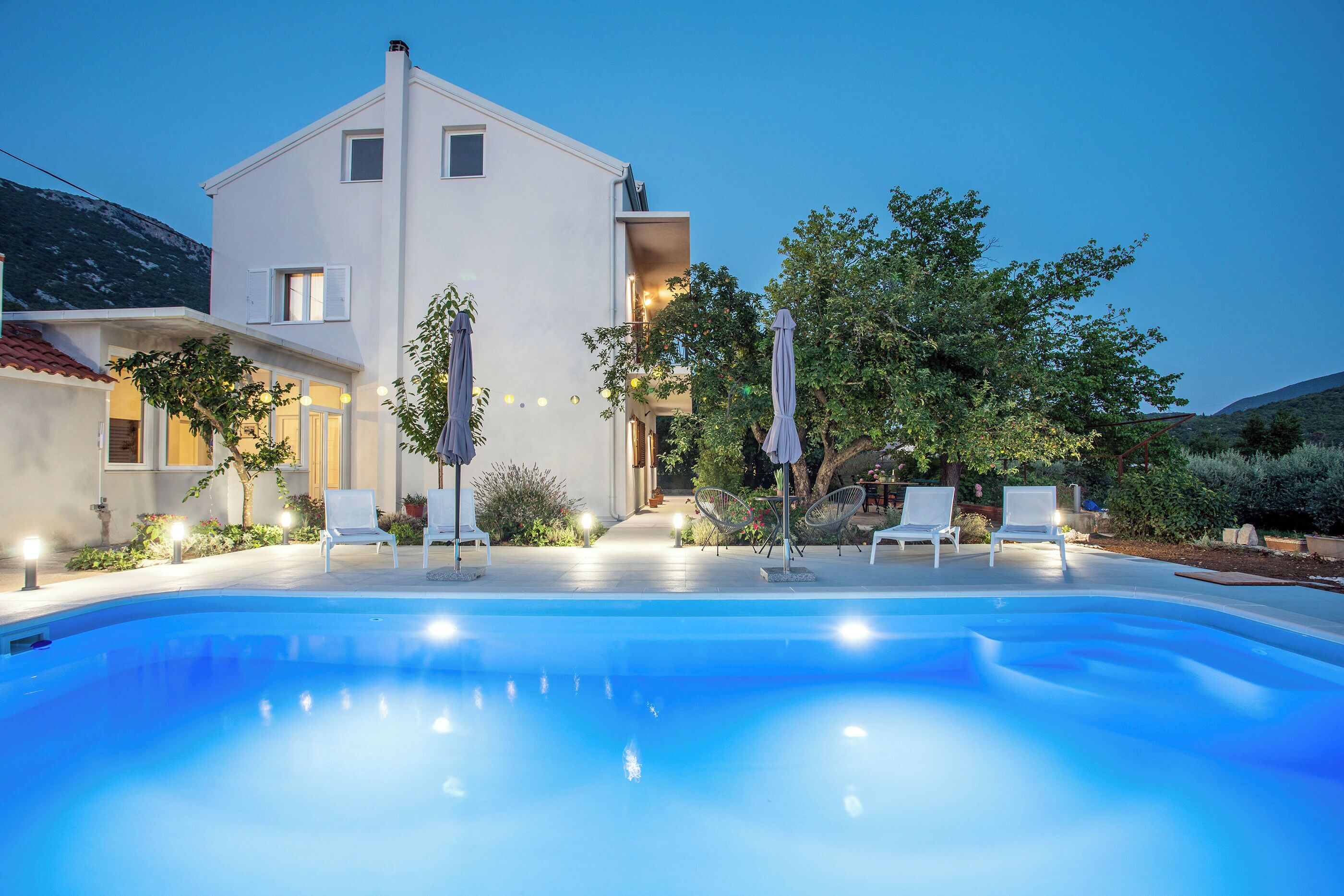 A modern house with a swimming pool, outdoor seating, and a well-lit garden.