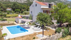 Uma casa moderna de dois andares com piscina, rodeada por vegetação exuberante e montanhas ao fundo.