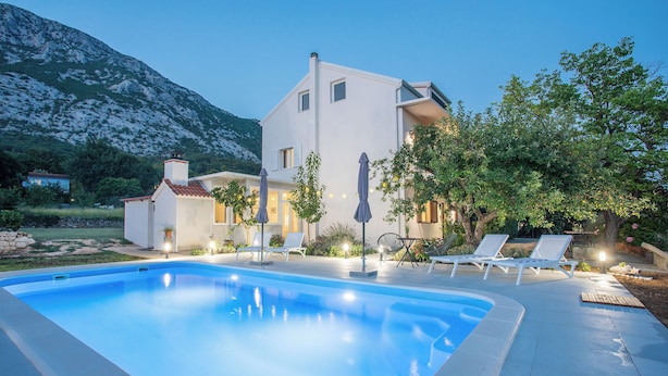 Uma villa moderna com piscina, área de estar externa e paisagem montanhosa ao fundo.