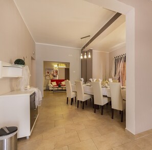 A modern dining area with a white table set for four, a red sofa, and a kitchen area in the background. - Villa Spacious (Zminj)