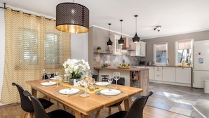 A modern kitchen with white cabinets, a wooden dining table set for six, and pendant lighting. - Villa Arba (Rab)