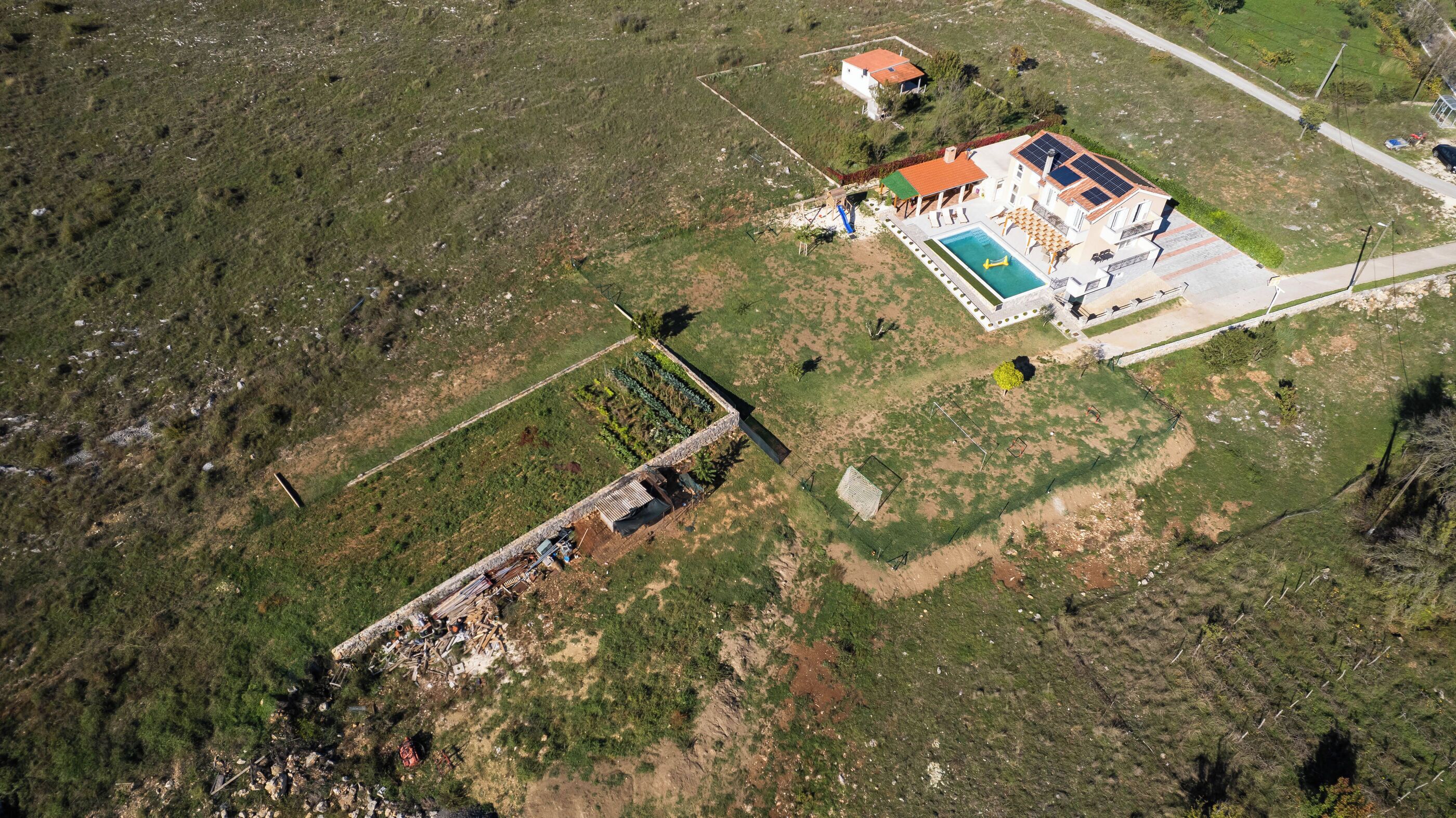 An aerial view of a property with a swimming pool, solar panels, and a fenced garden area.