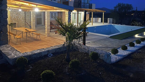 Ett modernt hus med en swimmingpool, stenmurar och en uteplats med utemöbler.