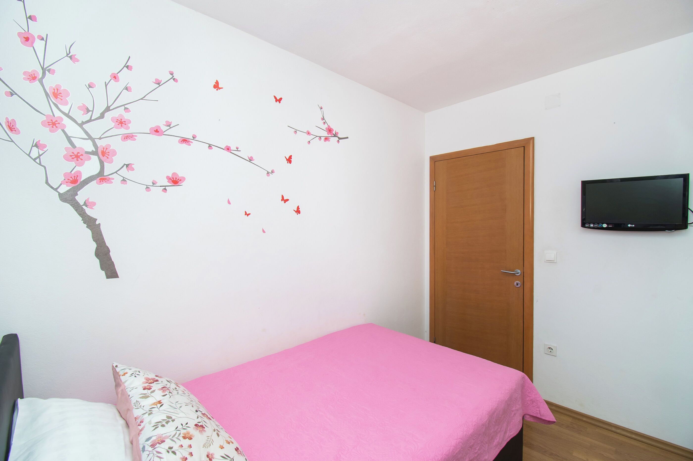 A bedroom with a bed, a wooden door, and a wall-mounted TV.