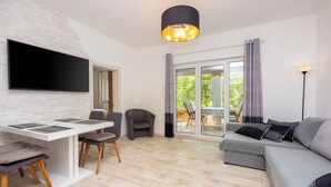 A modern living room with a flat-screen TV, a dining area with a white table and chairs, and a grey sofa. - Villa Mayer (Crikvenica)