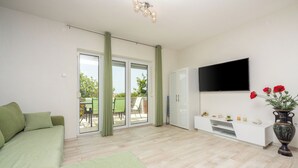 A modern living room with a sofa, a flat-screen TV, a white entertainment unit, and a sliding glass door leading to an outdoor area. - Villa Mayer (Crikvenica)