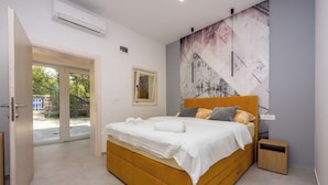 A bedroom with a bed, a nightstand, a wall-mounted air conditioner, a window, and a door. - Villa Mayer (Crikvenica)