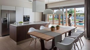 A modern kitchen with a central island, white chairs, and a dining table. - Villa Royal Green (Rasa)