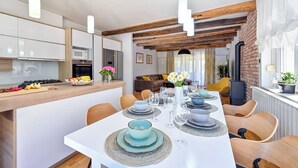 A modern kitchen with white cabinets, a wooden countertop, and a dining area with a white table set for six. - Villa Home2b (Bjelovar)