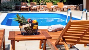 A poolside area with wooden lounge chairs, a pool, and a fruit basket on a table. - Villa Home2b (Bjelovar)