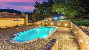A swimming pool with a stone wall and a grassy area with lounge chairs. - Villa Eirene (Kraljevica)