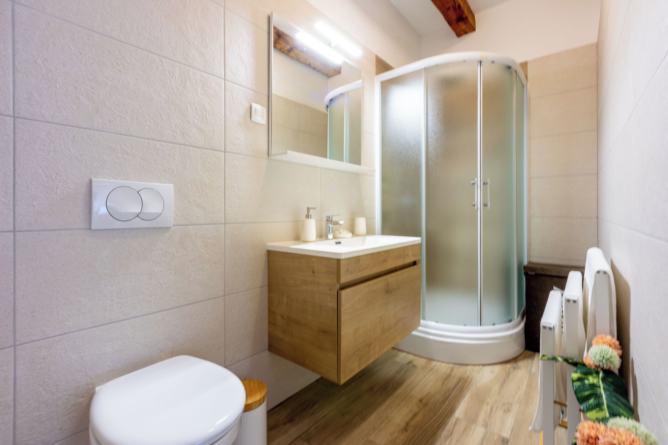 A modern bathroom with a toilet, wooden vanity, glass shower enclosure, and a mirror.