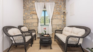 A cozy room with wicker furniture, a stone wall, and a window with white curtains. - Villa Eirene (Kraljevica)