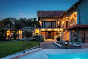 Une maison à deux étages avec une piscine, une façade en pierre et un espace extérieur aménagé pour se détendre.