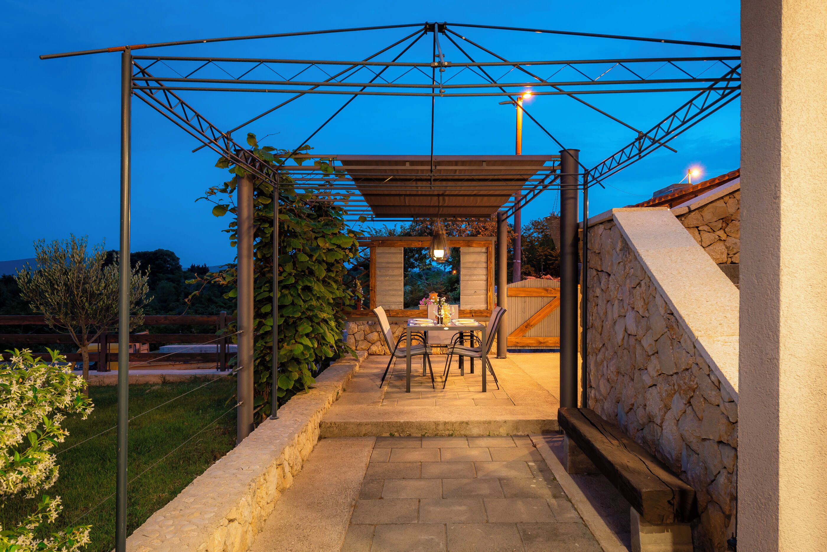 Un patio al aire libre con pérgola, paredes de piedra y una mesa con sillas.