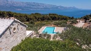 Un edificio in pietra con piscina, circondato da alberi e vista sul mare e sulle montagne.
