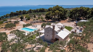 Un edificio in pietra con piscina, immerso tra alberi e vista sul mare.