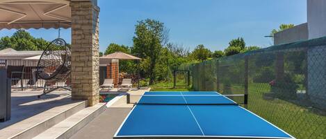 An outdoor ping pong table with a netted enclosure, stone pillars, and outdoor furniture.