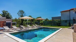 Una piscina rettangolare con acqua cristallina e blu, circondata da un solarium piastrellato. Lungo il bordo della piscina, ci sono lettini e ombrelloni.