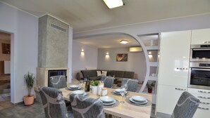 Una moderna zona pranzo con un tavolo in legno imbandito per sei persone, circondato da sedie grigie rivestite. Si nota un forno a incasso alla destra.
