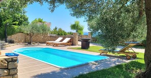 Une piscine avec des chaises longues, un mur en pierre et une vue sur la mer.