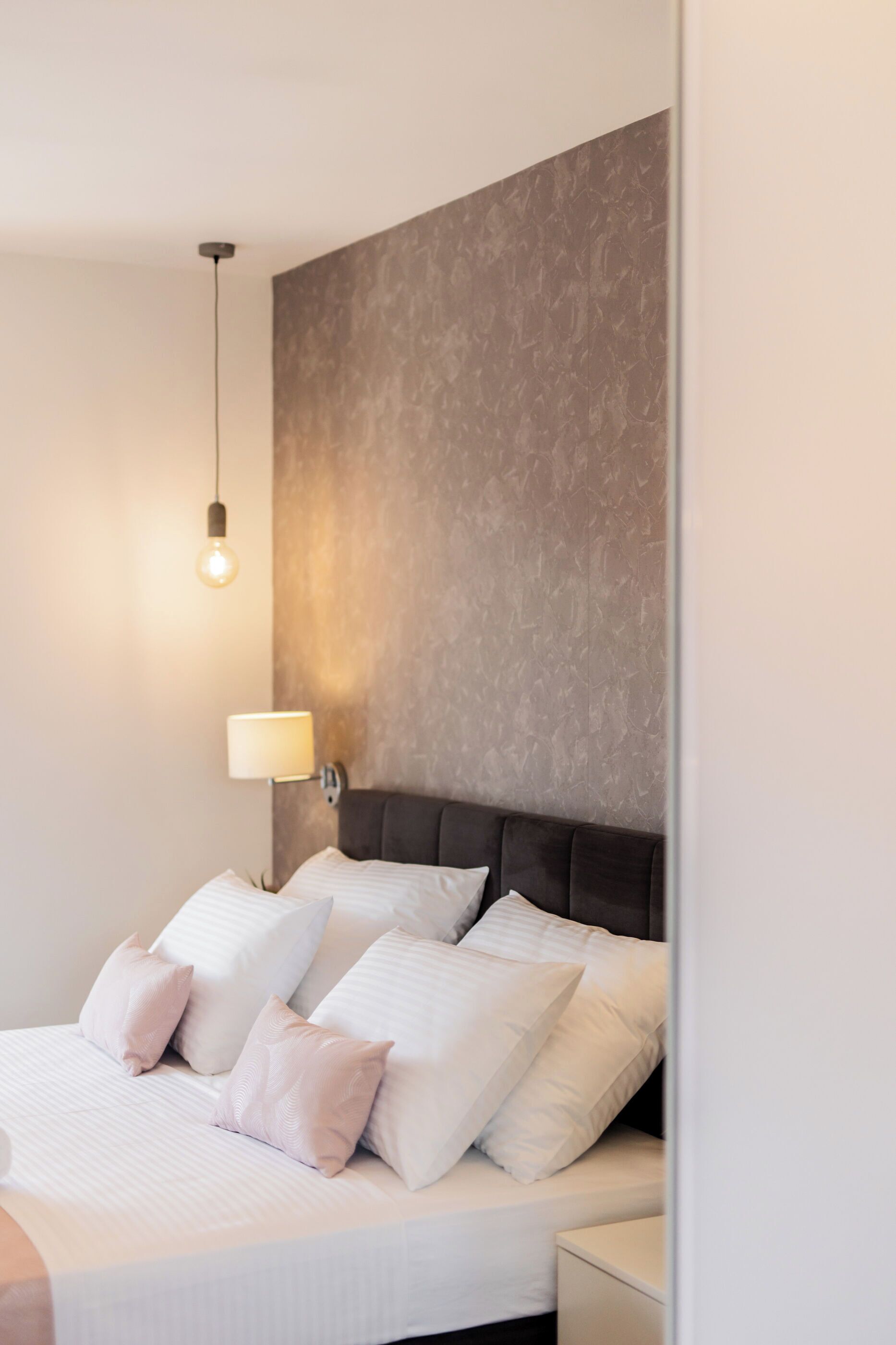 A modern bedroom with a large bed, a headboard, a wall-mounted lamp, and a bedside table.