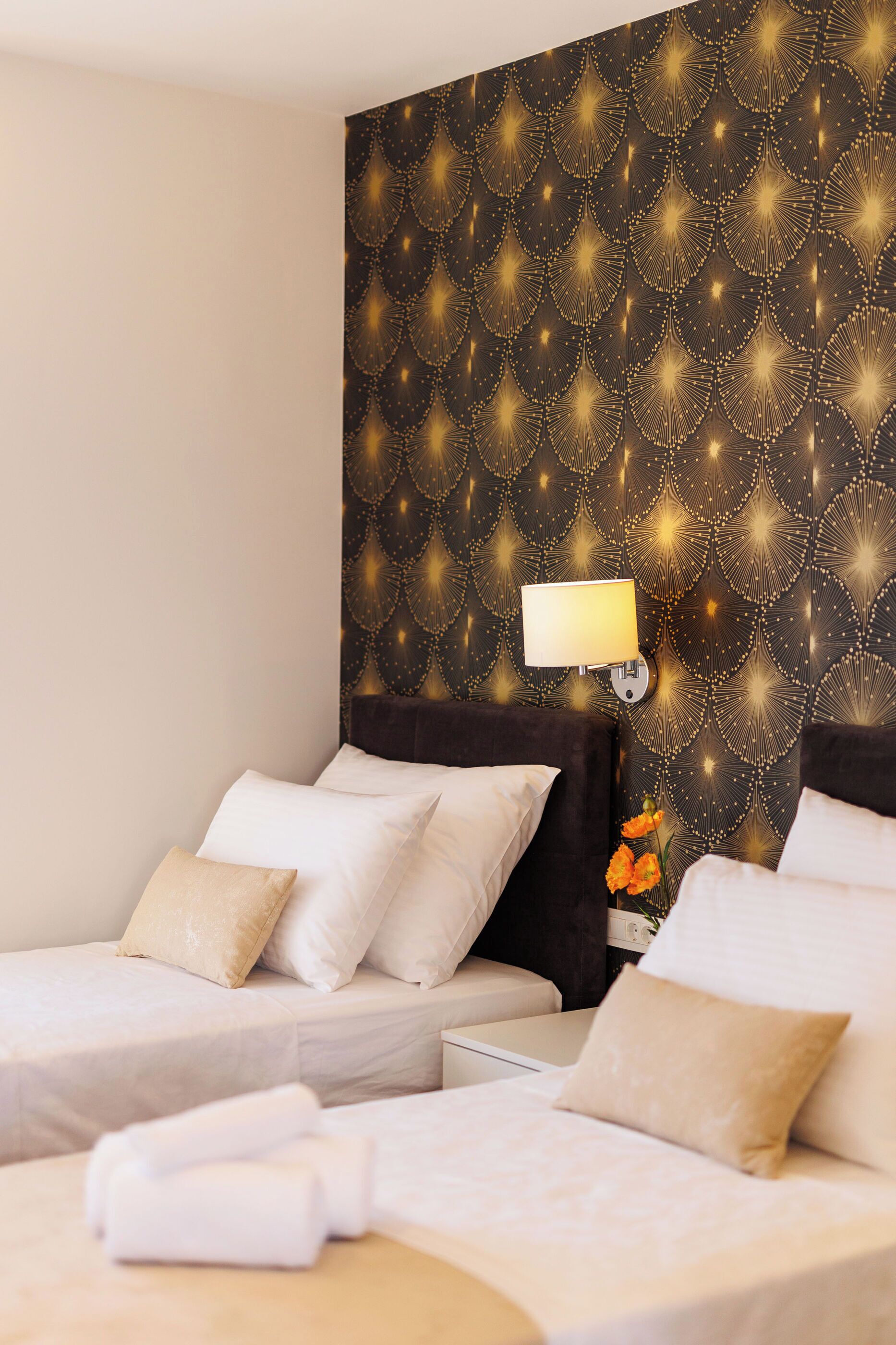 Une chambre d’hôtel avec deux lits, une lampe fixée au mur et un motif décoratif sur le mur.
