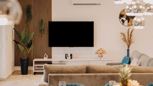 A modern living room with a flat-screen TV, a dining table set with plates and glasses, a sofa, and a potted plant. - Villa Dal' Mares (Marina)