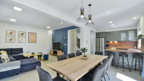 Una sala de estar moderna con un sofá, una mesa de comedor y una cocina con refrigerador y taburetes de bar.