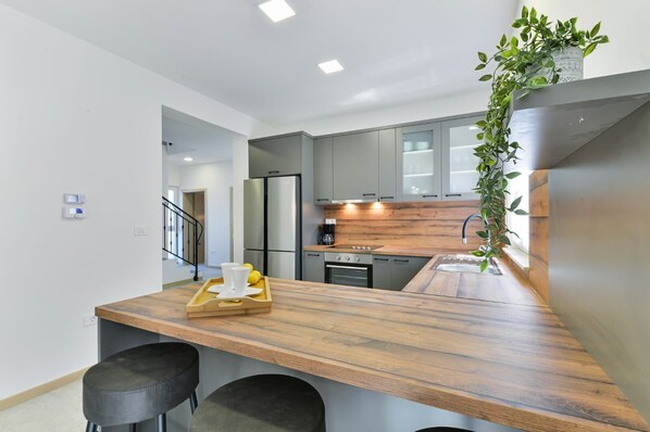 Une cuisine moderne avec un îlot central en bois, des appareils électroménagers en acier inoxydable et une plante suspendue.
