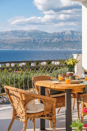 Un balcon agrémenté de fauteuils et d’une table en osier, offrant une vue sur un paysage montagneux et la mer.