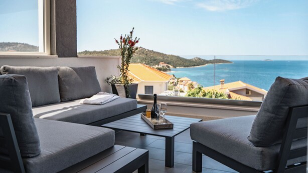 A balcony with a grey sofa, a small table, and a potted plant. - Villa Miracle (Rogoznica)