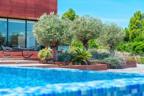 Una piscina con un edificio moderno al fondo, rodeada de diversos árboles y plantas.