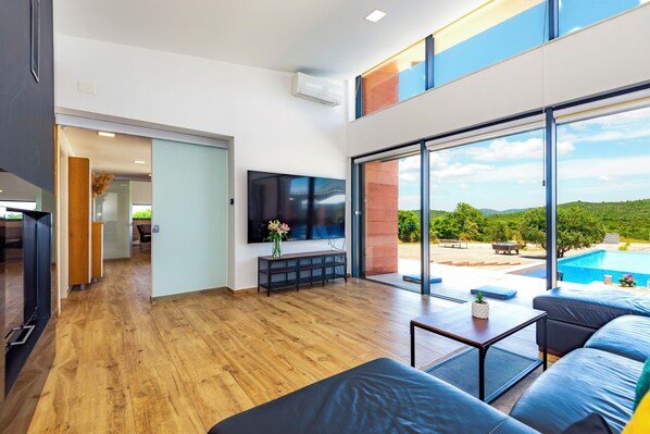 Una sala de estar moderna con un televisor grande, piso de madera y vista a una piscina.