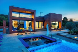 Una casa moderna con piscina, mobiliario de exterior y un patio bien iluminado.