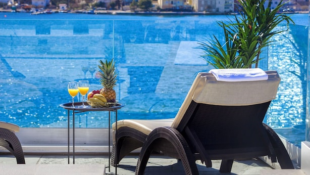 Un balcon avec un fauteuil en osier, une petite table avec des fruits et des boissons, et une vue sur la mer.